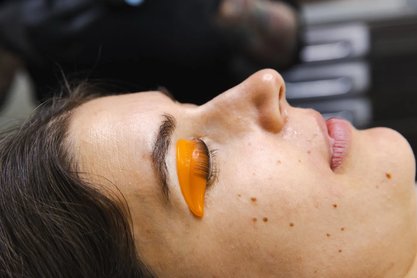 Perfil del ojo de una cliente con las pestañas peinadas hacia arriba sobre un molde de silicona naranja.